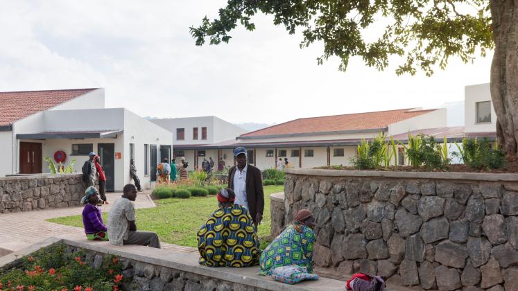 Photo of Butaro District Hospital, Photo by Iwan Baan, Visitors gather on a stone bench near the hospital
